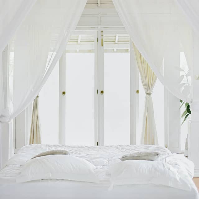 white sheer curtains behind bed with white linens