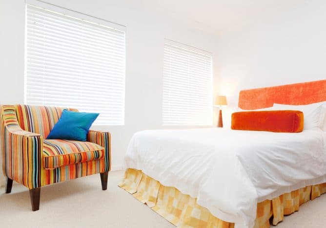 venetian blind in brightly light bedroom with orange and blue furnishings and white bed spread